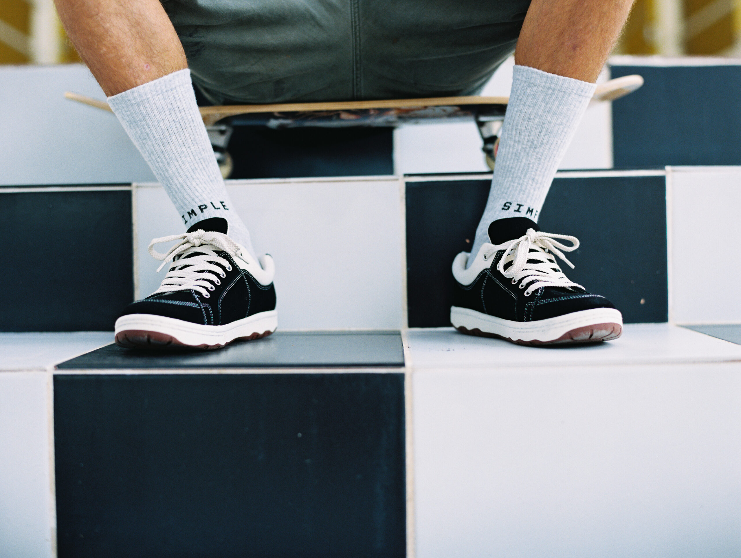 Model sitting on skateboard wearing shoes cropped at feet on checkered staircase